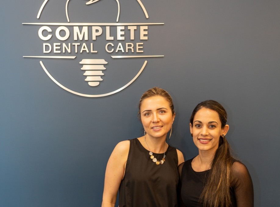 Two women smiling in front of Complete Dental Care sign on wall