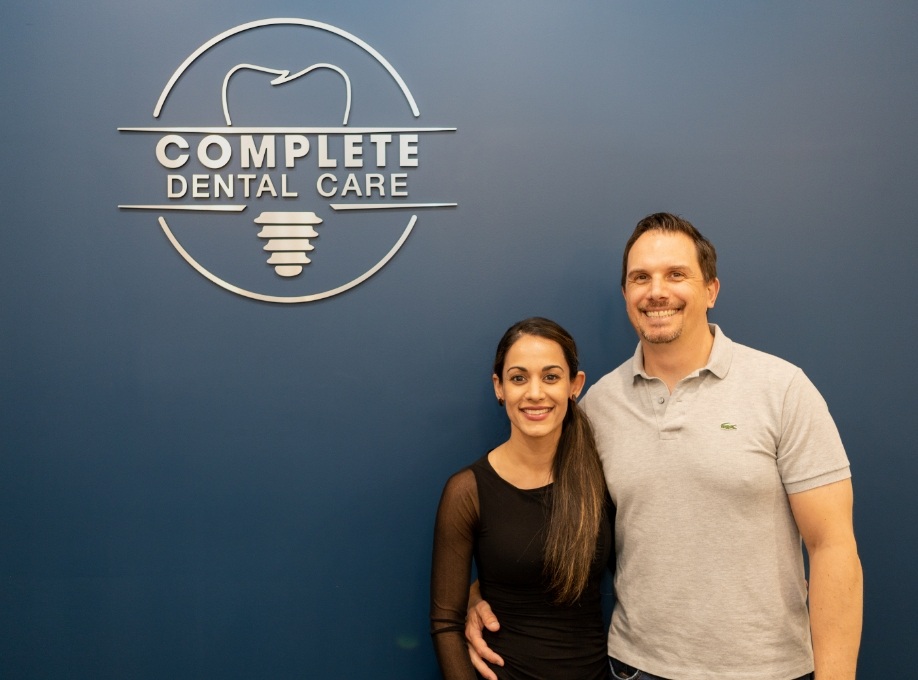 Man and woman smiling in front of Complete Dental Care sign on wall