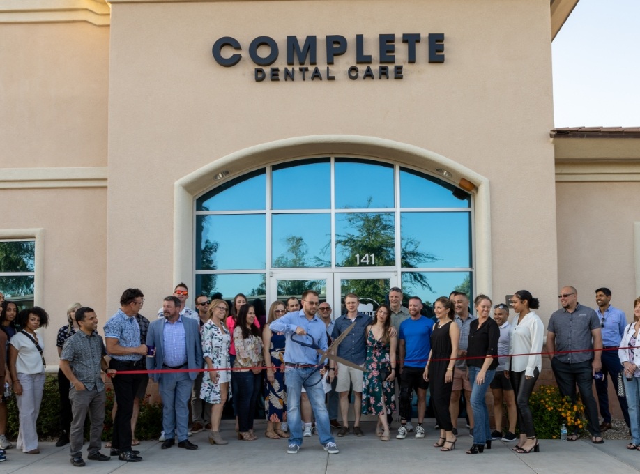 Doctor Rodda cutting ribbon with giant scissors in front of Complete Dental Care