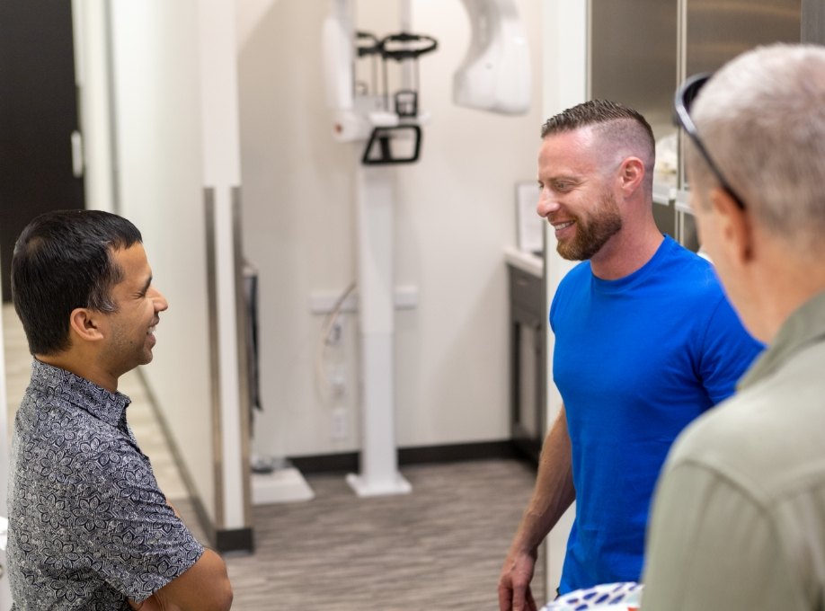 Three men talking with C T dental scanner against wall in background