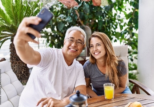 Man and woman taking selfie outdoors while eating breakfast