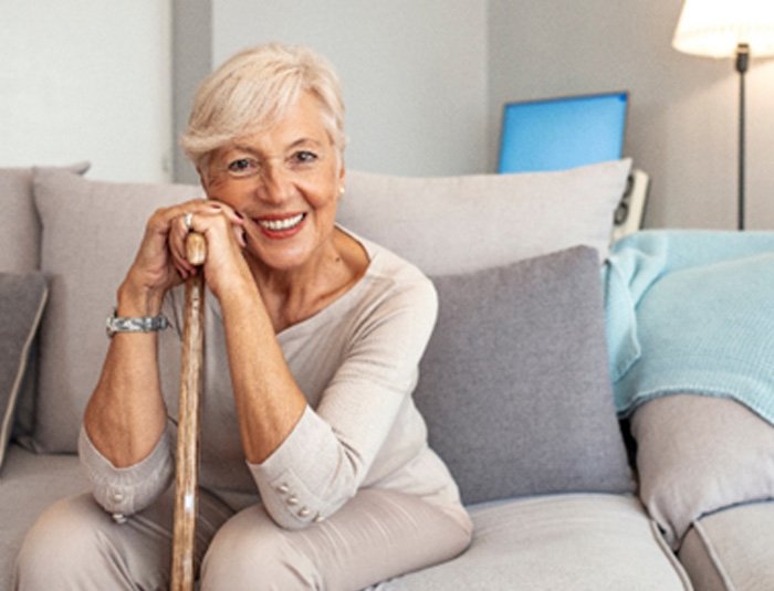 A smiling senior woman sitting on a couch with a cane