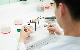 Lab tech building dentures on plaster mold.