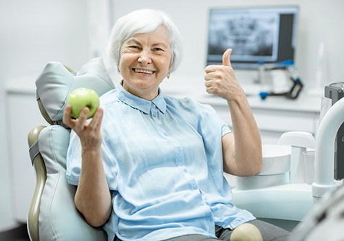 Dental patient holding apple and giving thumbs up