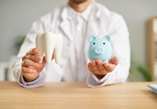a dentist holding a model tooth and a piggy bank