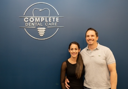 Smiling man and woman in front of Complete Dental Care sign on wall