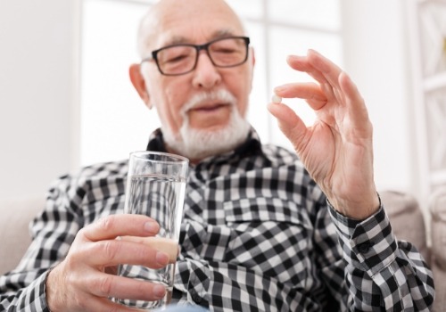 Senior man holding a pill and a glass of water